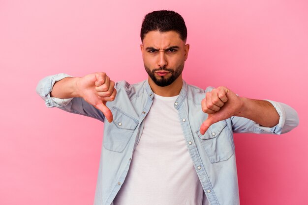 Hombre joven de raza mixta aislado en rosa mostrando el pulgar hacia abajo y expresando aversión.