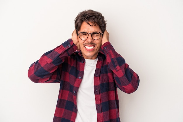 Hombre joven de raza mixta aislado sobre fondo blanco cubriendo las orejas con las manos.