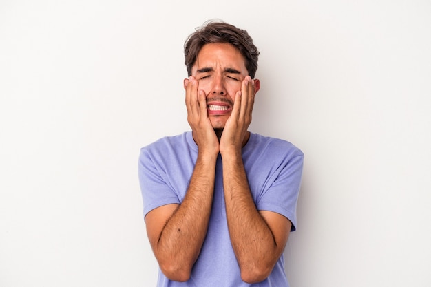 Hombre joven de raza mixta aislado sobre fondo blanco llorando, descontento con algo, concepto de agonía y confusión.