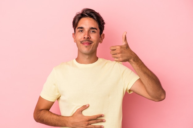 Hombre joven de raza mixta aislado sobre fondo blanco toca la barriga, sonríe suavemente, comiendo y concepto de satisfacción.