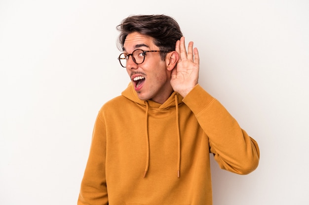 Hombre joven de raza mixta aislado sobre fondo blanco tratando de escuchar un chisme.