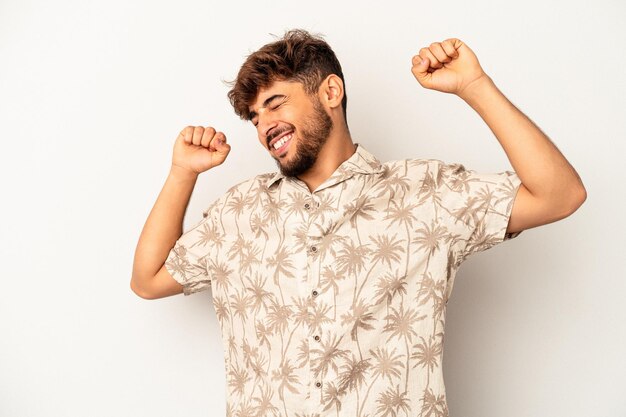 Hombre joven de raza mixta aislado sobre fondo gris celebrando un día especial, salta y levanta los brazos con energía.