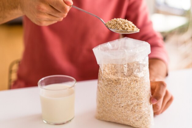 Hombre joven de raza mixta comiendo avena y leche para el desayuno en su cocina