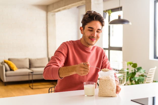 Hombre joven de raza mixta comiendo avena y leche para el desayuno en su cocina