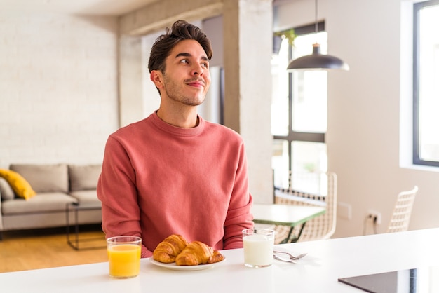 Hombre joven de raza mixta desayunando en una cocina en la mañana soñando con lograr metas y propósitos