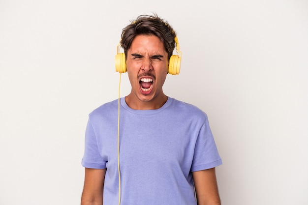 Hombre joven de raza mixta escuchando música aislada sobre fondo azul gritando muy enojado y agresivo.