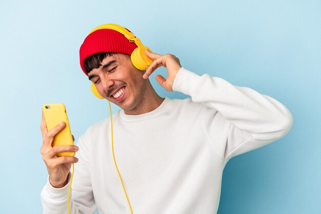 Hombre joven de raza mixta escuchando música aislado sobre fondo azul.