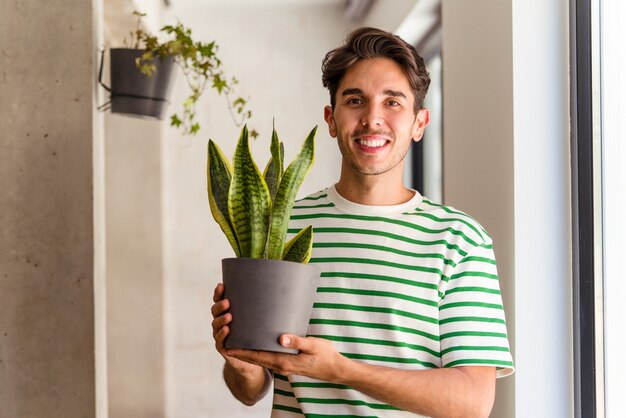 Hombre joven de raza mixta con una planta en su casa