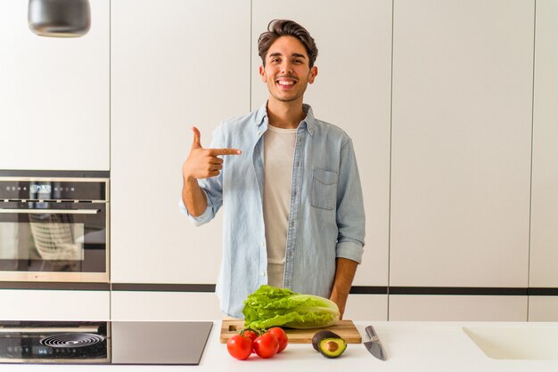 Hombre joven de raza mixta preparando una ensalada para el almuerzo persona apuntando con la mano a un espacio de copia de camisa, orgulloso y seguro