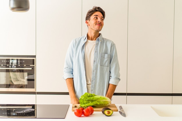 Hombre joven de raza mixta preparando una ensalada para el almuerzo soñando con lograr metas y propósitos