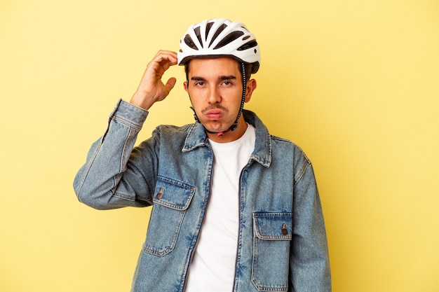 Hombre joven de raza mixta que llevaba un casco de bicicleta aislado sobre fondo amarillo conmocionado, ella ha recordado una reunión importante.