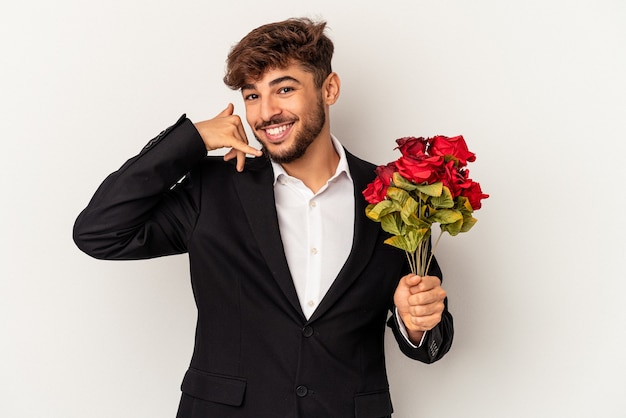 Hombre joven de raza mixta con ramo de rosas aislado sobre fondo blanco mostrando un gesto de llamada de teléfono móvil con los dedos.