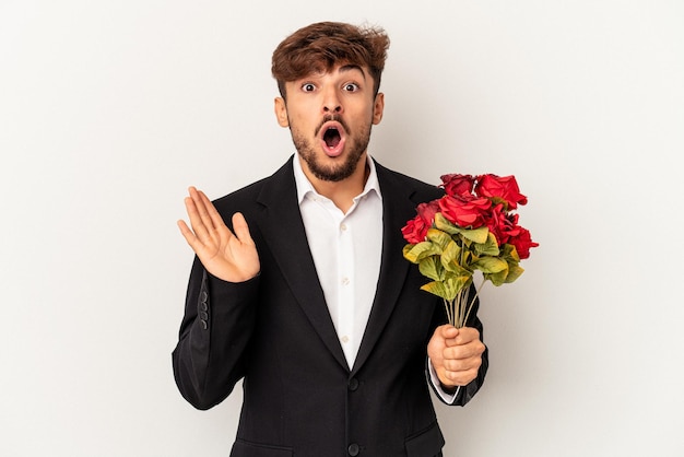 Hombre joven de raza mixta con ramo de rosas aislado sobre fondo blanco sorprendido y consternado.