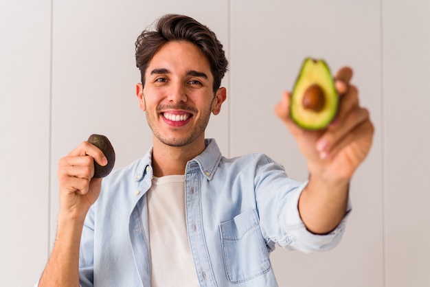 Hombre joven de raza mixta sosteniendo aguacates en su cocina