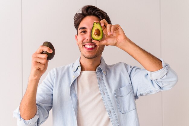 Hombre joven de raza mixta sosteniendo aguacates en su cocina