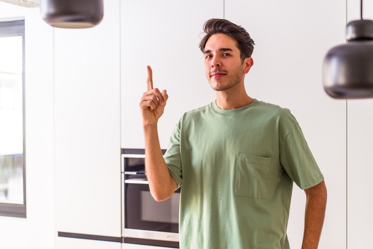 Foto hombre joven de raza mixta en su cocina mostrando el número uno con el dedo.