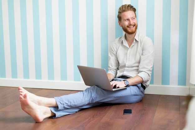 Hombre joven redhair sentado en el suelo y trabajando en la computadora portátil