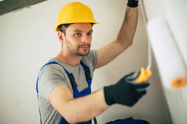 Hombre joven de reparación de viviendas o trabajador ocupado con la renovación de la casa, sostiene equipos de construcción, viste ropa de trabajo informal en la nueva construcción