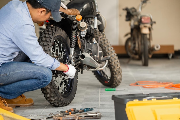 Hombre joven reparando motocicleta en garaje de taller Hombre reparando motocicleta en taller de reparación Hobby mecánico y conceptos de reparación