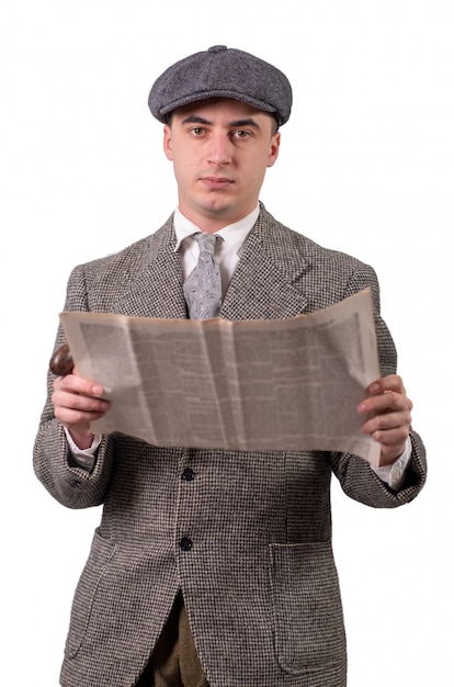 Hombre joven en ropa vintage con sombrero, leyendo el periódico