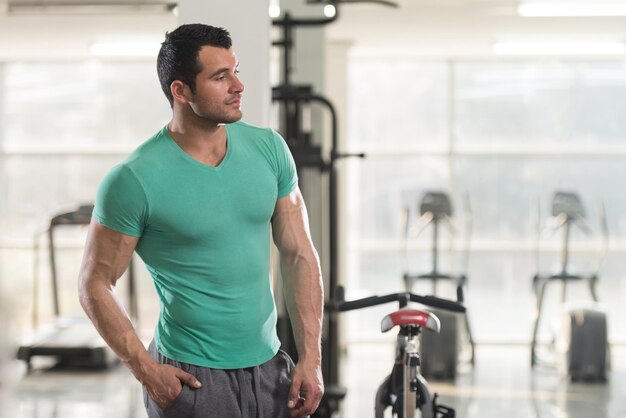 Hombre joven sano en camiseta de pie fuerte y flexionando los músculos Muscular culturista atlético modelo de fitness posando después de los ejercicios