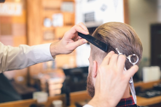 Hombre joven sentado en una barbería mientras peluquero cortando el cabello