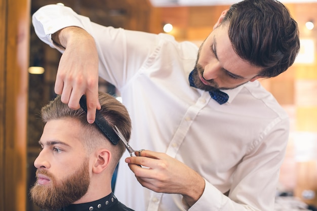 Hombre joven sentado en una barbería mientras peluquero cortando el cabello