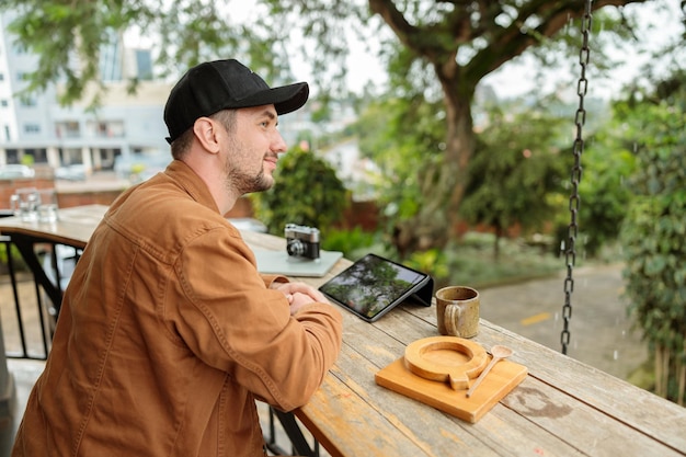 Foto hombre joven sentado en un café y trabajando en línea al aire libre