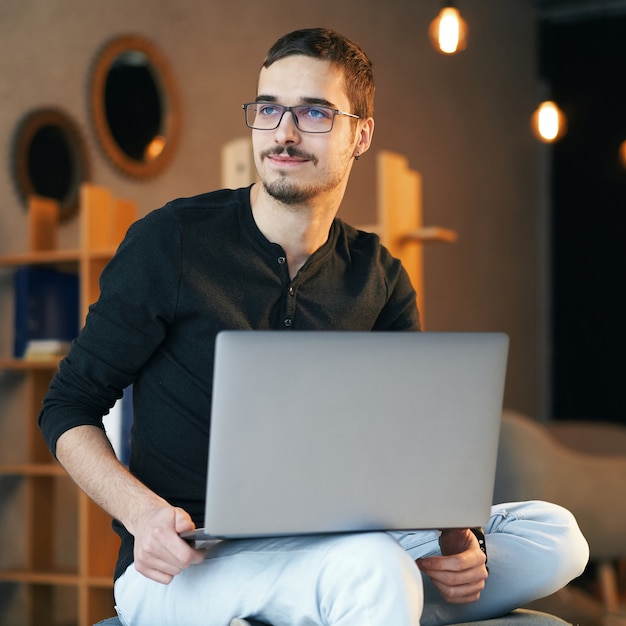 Hombre joven sentado con la computadora. Freelancer en gafas trabajando con laptop, gerente de proyectos.