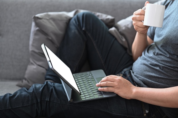 Hombre joven sentado en el sofá y usando la tableta de la computadora.