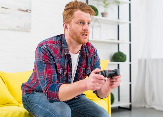 Foto hombre joven serio que juega al juego con el controlador de video en casa