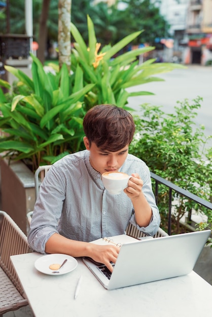 Hombre joven serio que usa una computadora portátil para trabajar al aire libre