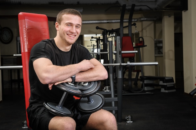 El hombre joven se sienta después de entrenamiento en gimnasio