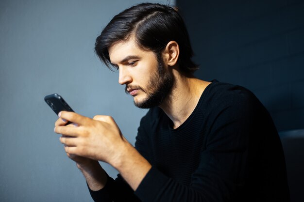 Hombre joven con smartphone en el fondo de la pared gris y negra.