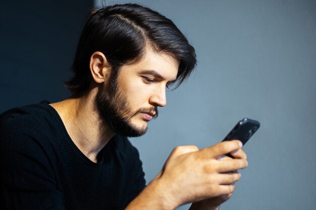 Hombre joven con smartphone en el fondo de la pared gris y negra.