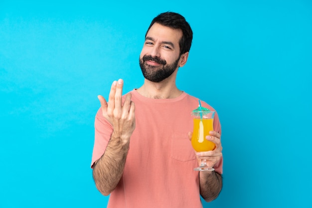 Hombre joven sobre la celebración de un cóctel sobre la pared azul aislada que invita a venir con la mano. Feliz de que hayas venido