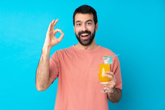 Hombre joven sobre la celebración de un cóctel sorprendido y mostrando signo ok