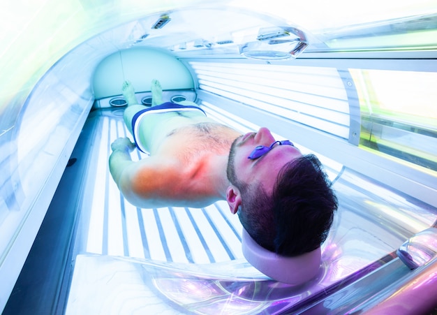 Hombre joven en el solarium en salón de belleza.