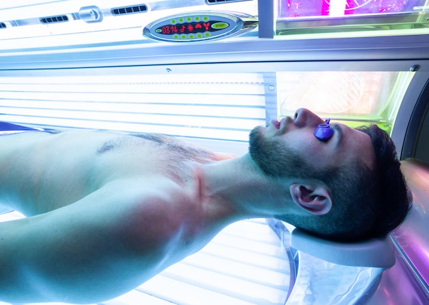 Hombre joven en el solarium en salón de belleza.