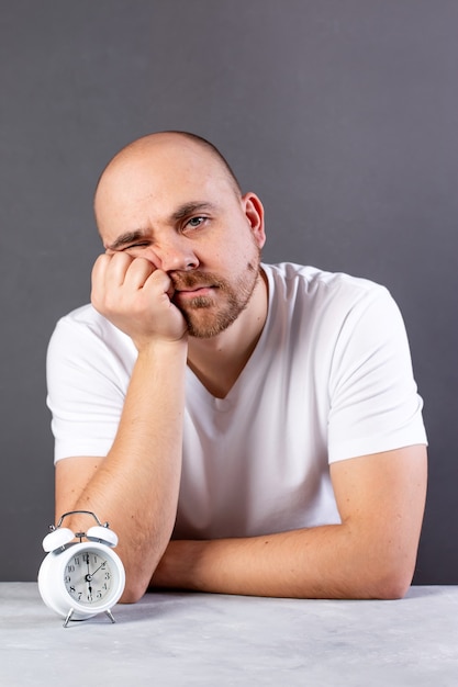 Hombre joven soñoliento sobre fondo gris con reloj despertador