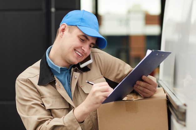 Hombre joven sonriente aceptando el pedido por teléfono y haciendo la entrega