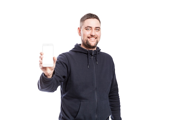 El hombre joven sonriente lindo muestra un teléfono con una pantalla aislada. Aislado en blanco