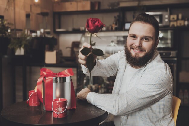 Hombre joven sonriente que sienta la tabla que sostiene una rosa