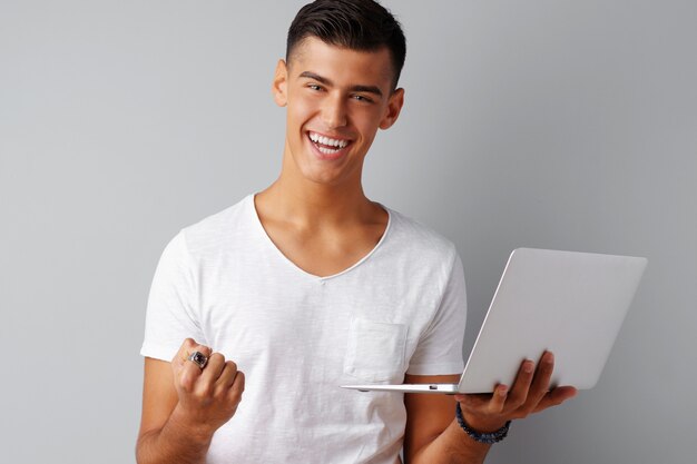 Hombre joven sonriente que sostiene el ordenador portátil