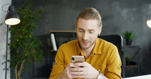 Hombre joven sonriente que sostiene smartphone en manos en oficina.