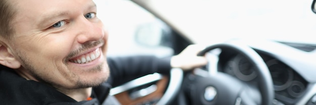 Hombre joven sonriente se sienta en el salón del coche detrás del volante