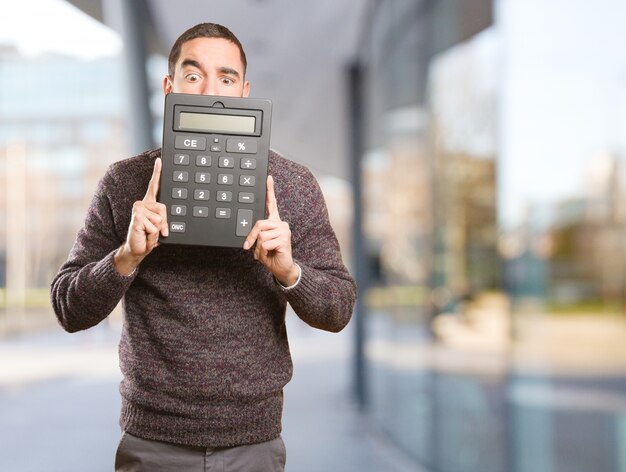 Hombre joven sorprendido que sostiene una calculadora