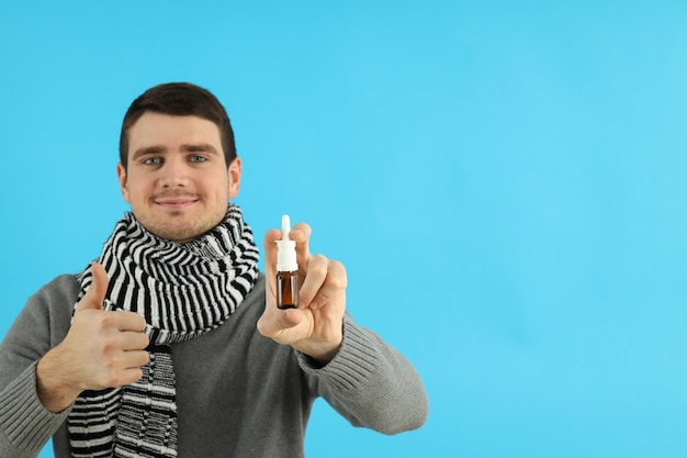 Hombre joven con spray nasal sobre fondo azul, concepto de secreción nasal