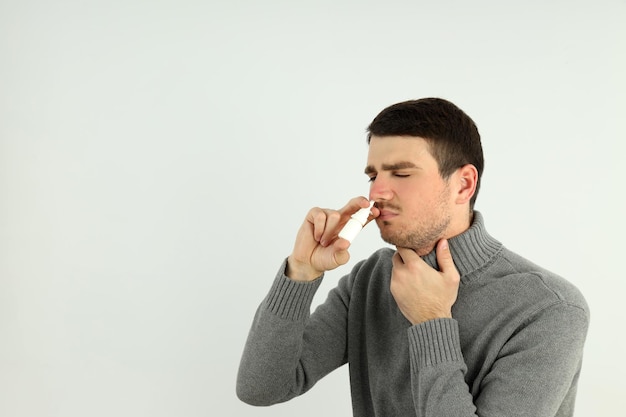 Hombre joven con spray nasal sobre fondo claro, concepto de secreción nasal