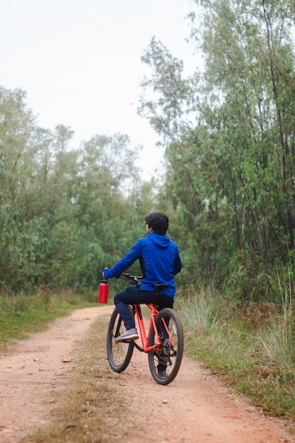 Hombre joven en su bicicleta en un camino forestal, practicando deportes en la naturaleza.